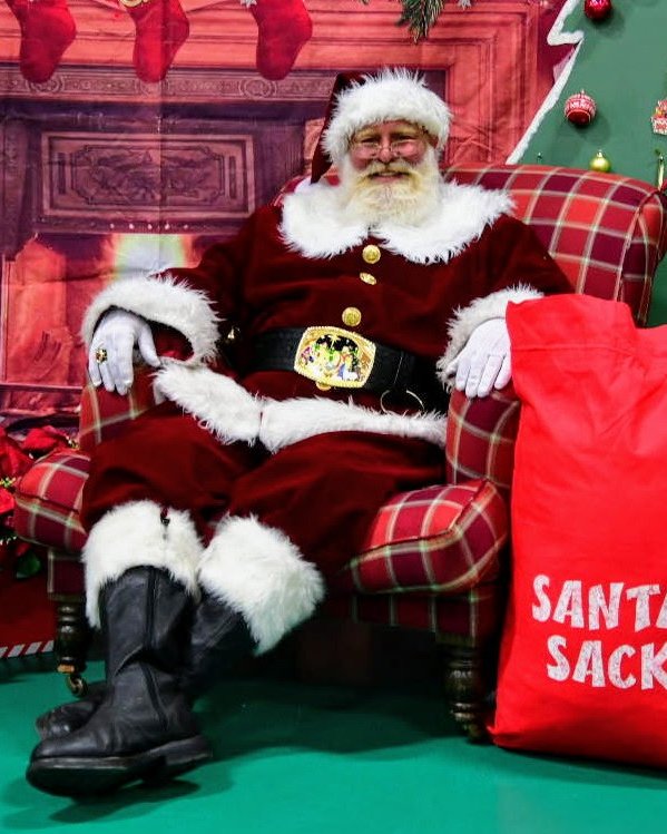 Santa Tony smiling in a plaid armchair beside his Santa Sack